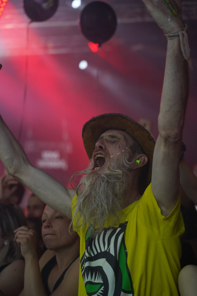 Un festivalier avec un chapeau crie et lève les bras vers le haut