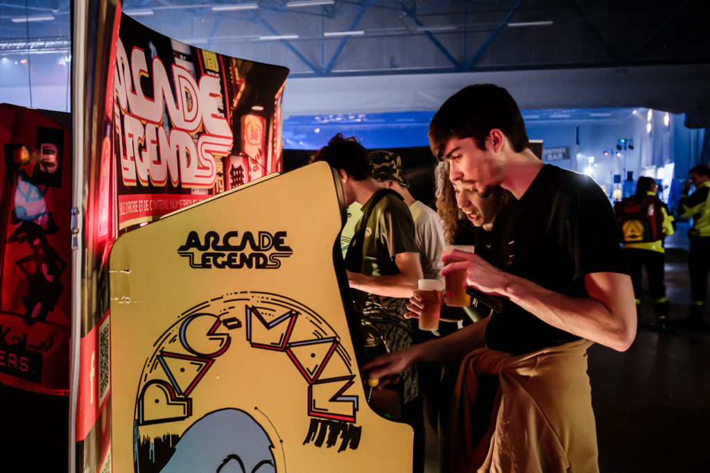 Des festivaliers jouent &agrave; des bornes d'arcade avec des bi&egrave;res